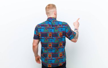 Havalı bir tişört giyen genç sarışın adam fotokopi alanındaki objeyi işaret ediyor. Arka plan beyaz.