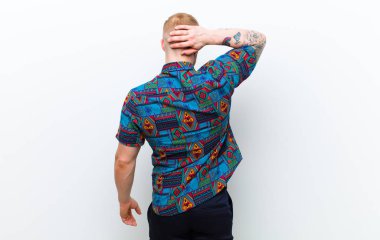 Havalı bir tişört giyen genç sarışın adam, neşeli bir şekilde gülümsüyor, mutlu hissediyor ve yan ve yukarı doğru işaret ediyor, fotokopi alanındaki nesneleri beyaz arka planda gösteriyor.