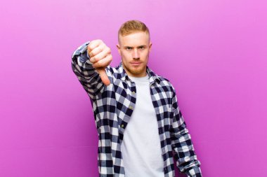 Kare gömlekli genç sarışın adam kızgın, sinirli, hayal kırıklığına uğramış ya da hoşnutsuz, ciddi bir bakışla başparmağını kaldırıyor.