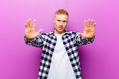 Kare gömlekli genç sarışın adam ciddi, mutsuz, sinirli ve hoşnutsuz görünüyor ya da her iki avuçta da dur diyor.