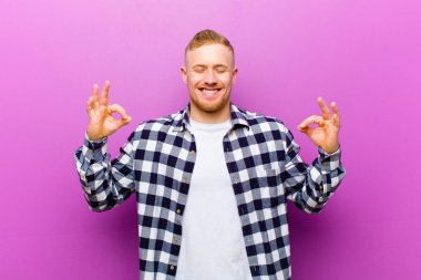 Kare gömlekli genç sarışın adam konsantre ve meditasyon yapıyor, tatmin oluyor ve rahatlıyor, düşünüyor ya da bir seçim yapıyor.