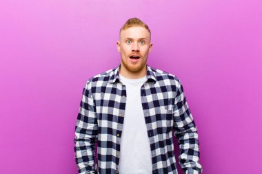 Kare gömlekli genç sarışın adam şok olmuş ya da şaşırmış görünüyor, ağzı açık bir şekilde 