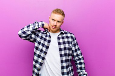 Kare gömlekli genç sarışın adam stresli, endişeli, yorgun ve hayal kırıklığına uğramış, gömleğini çekiştirip duruyor.