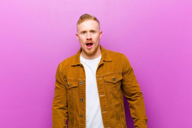 Genç sarışın adam korkmuş ve şok olmuş hissediyor, ağzı açık mor arka plana karşı şaşkınlık içinde.