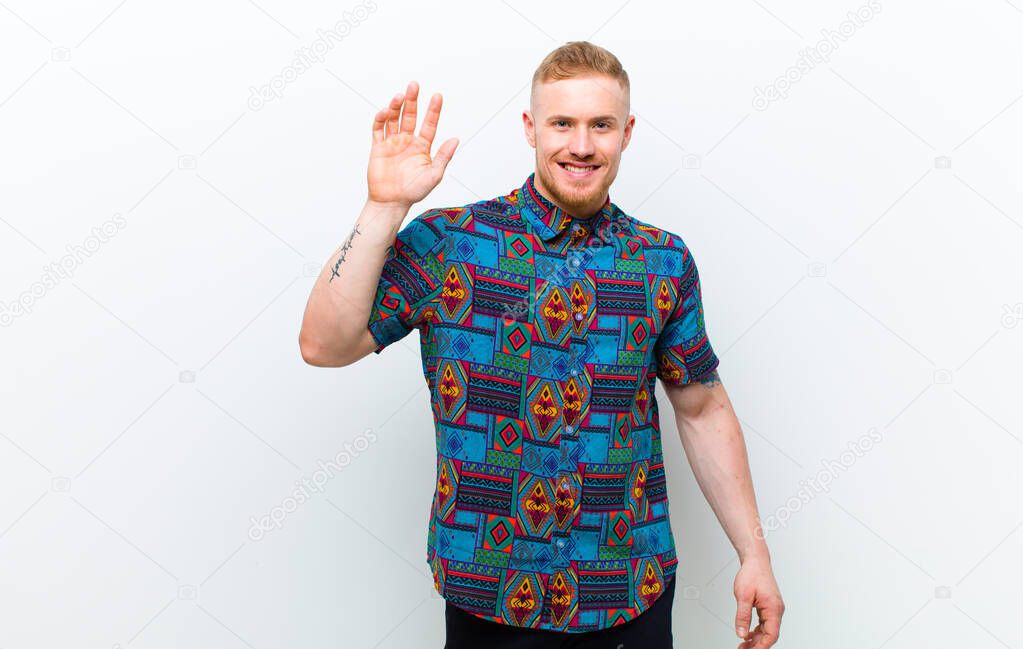 young blonde man wearing a cool shirt smiling happily and cheerfully, waving hand, welcoming and greeting you, or saying goodbye against white background
