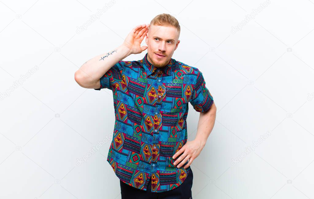 young blonde man wearing a cool shirt smiling, looking curiously to the side, trying to listen to gossip or overhearing a secret against white background