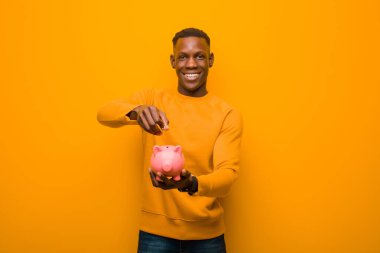 Genç Afrikalı Amerikalı siyah adam turuncu duvara karşı domuz kumbarası ile