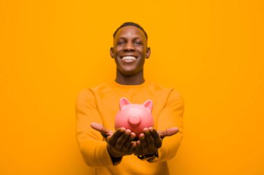 Genç Afrikalı Amerikalı siyah adam turuncu duvara karşı domuz kumbarası ile