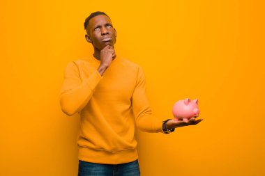 Genç Afrikalı Amerikalı siyah adam turuncu duvara karşı domuz kumbarası ile