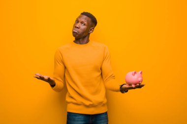 Genç Afrikalı Amerikalı siyah adam turuncu duvara karşı domuz kumbarası ile