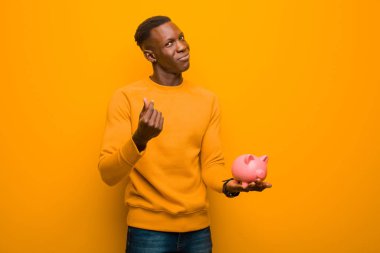 Genç Afrikalı Amerikalı siyah adam turuncu duvara karşı domuz kumbarası ile
