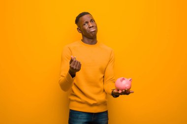 Genç Afrikalı Amerikalı siyah adam turuncu duvara karşı domuz kumbarası ile