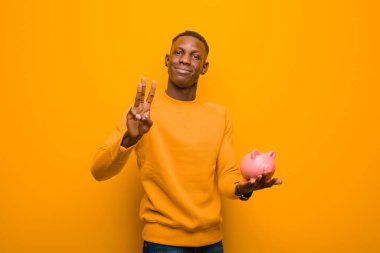 Genç Afrikalı Amerikalı siyah adam turuncu duvara karşı domuz kumbarası ile