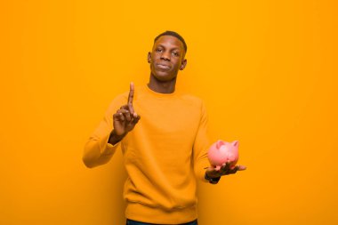 Genç Afrikalı Amerikalı siyah adam turuncu duvara karşı domuz kumbarası ile