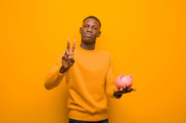 Genç Afrikalı Amerikalı siyah adam turuncu duvara karşı domuz kumbarası ile