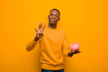 Genç Afrikalı Amerikalı siyah adam turuncu duvara karşı domuz kumbarası ile