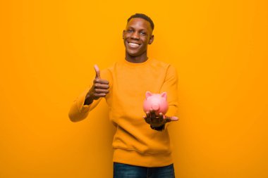 Genç Afrikalı Amerikalı siyah adam turuncu duvara karşı domuz kumbarası ile