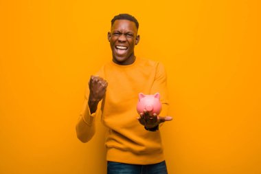 Genç Afrikalı Amerikalı siyah adam turuncu duvara karşı domuz kumbarası ile