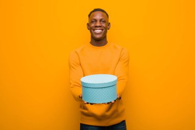 Genç Afro-Amerikan siyah adam turuncu duvara karşı bir hediyeyle