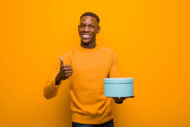 Genç Afro-Amerikan siyah adam turuncu duvara karşı bir hediyeyle