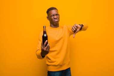 Genç Afrikalı Amerikalı siyahi adam turuncu duvara karşı bira içiyor.