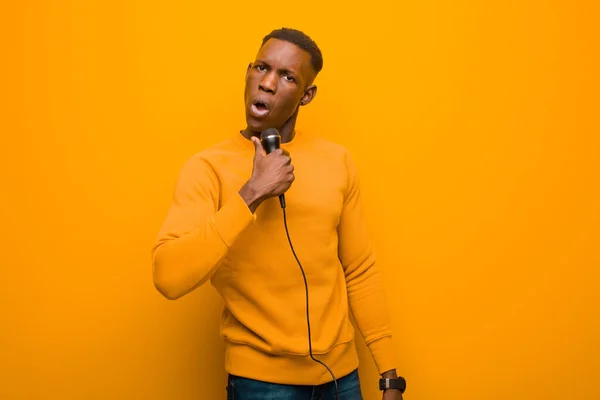 Νεαρός Αφροαμερικάνος Μαύρος Ενάντια Πορτοκαλί Τοίχο Μικρόφωνο — Φωτογραφία Αρχείου