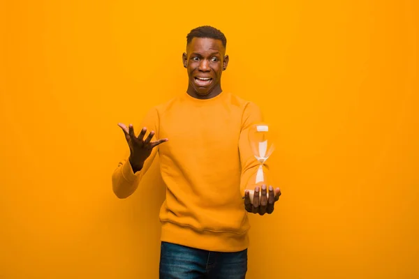 young african american black man against orange wall with a sand clock timer