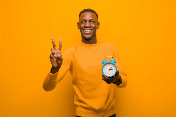 young african american black man against orange wall holding an alarm clock