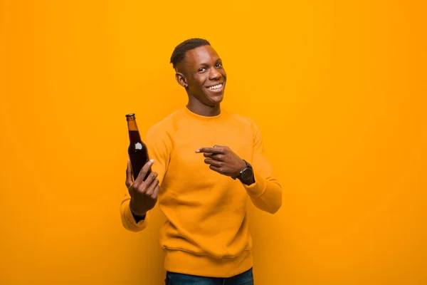 young african american black man against orange wall having a beer