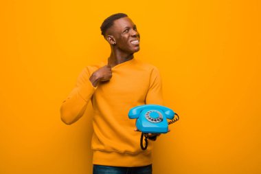 Genç Afro-Amerikan siyahi adam turuncu duvara karşı eski model bir telefonla