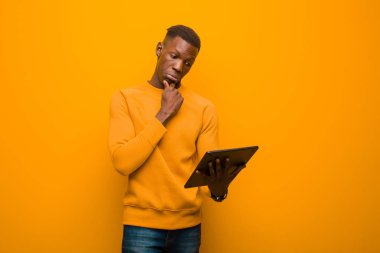 Genç Afro-Amerikan siyah adam turuncu duvara karşı akıllı bir tabletle