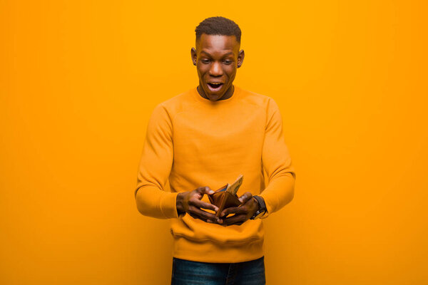 Young african american black man against orange wall, money concept.