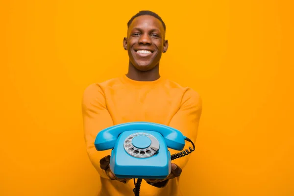 若いアフリカ系アメリカ人の黒人男性がオレンジの壁にヴィンテージの電話で — ストック写真