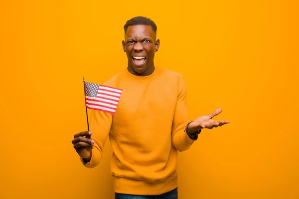 young african american black man against orange wall holding an usa flag