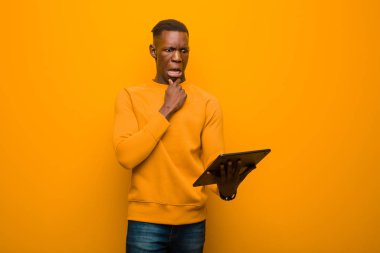 Genç Afro-Amerikan siyah adam turuncu duvara karşı akıllı bir tabletle