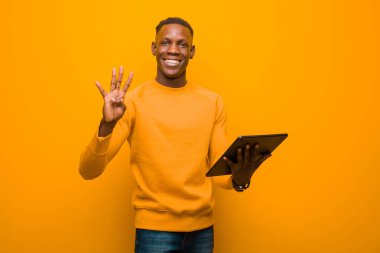 Genç Afro-Amerikan siyah adam turuncu duvara karşı akıllı bir tabletle