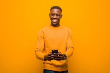 Genç Afro-Amerikan siyah adam turuncu duvara karşı akıllı bir telefonla