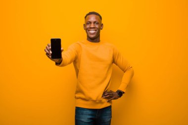 Genç Afro-Amerikan siyah adam turuncu duvara karşı akıllı bir telefonla