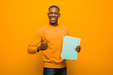 Genç Afro-Amerikan siyahi adam turuncu duvara karşı elinde kitapla