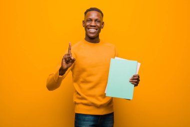 Genç Afro-Amerikan siyahi adam turuncu duvara karşı elinde kitapla