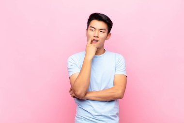 Şaşırmış, gergin, endişeli ya da korkmuş bakışları olan genç Çinli bir adam düz renkli duvara karşı fotokopi odasına doğru bakıyor.