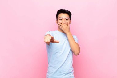 Genç Çinli adam sana gülüyor, kamerayı işaret ediyor ve seninle dalga geçiyor ya da seninle dalga geçiyor.