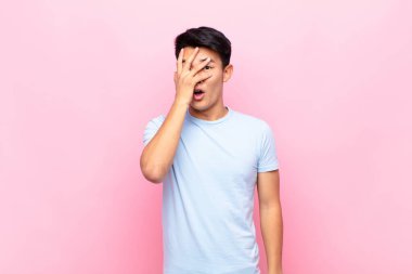 Genç Çinli adam şok olmuş, korkmuş ya da korkmuş görünüyordu. Yüzü elle kaplıydı ve parmaklarının arasından düz duvara bakıyordu.