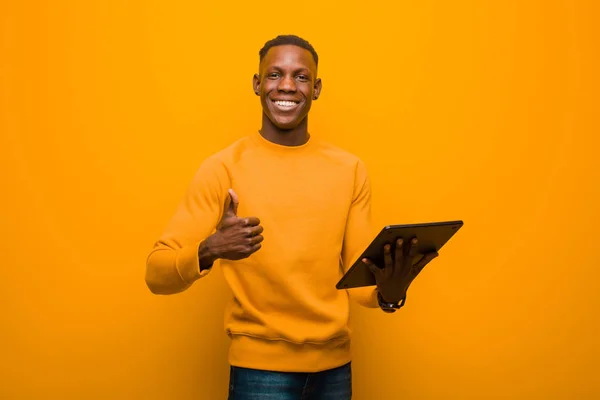 young african american black man against orange wall with a smart tablet