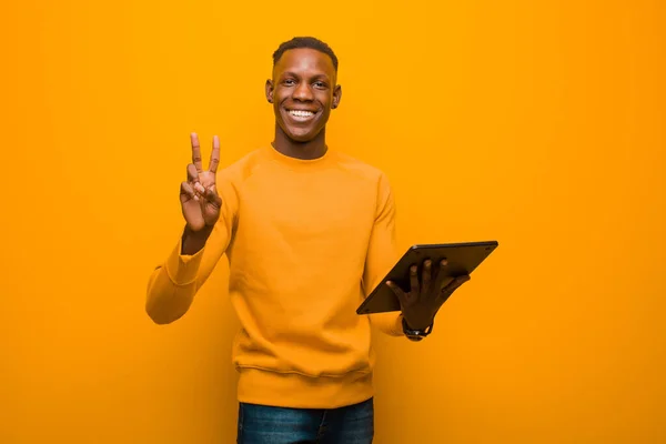 Joven Afroamericano Negro Hombre Contra Pared Naranja Con Una Tableta —  Fotos de Stock