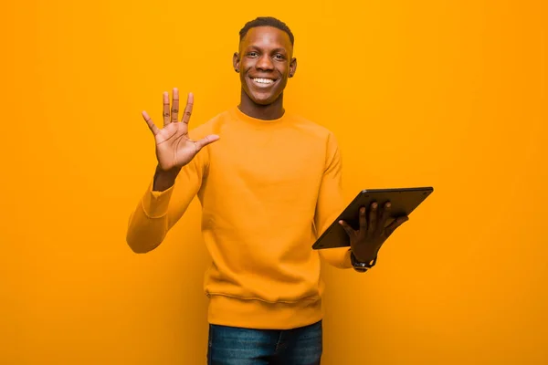 Νεαρός Αφροαμερικάνος Μαύρος Ενάντια Στον Πορτοκαλί Τοίχο Ένα Έξυπνο Tablet — Φωτογραφία Αρχείου