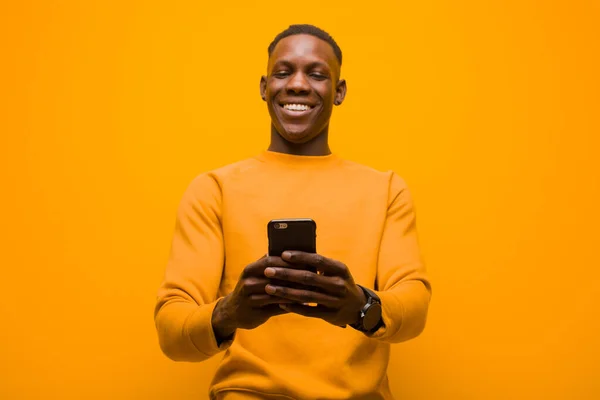若いアフリカ系アメリカ人の黒人男性がオレンジの壁にスマートフォンを向けて — ストック写真