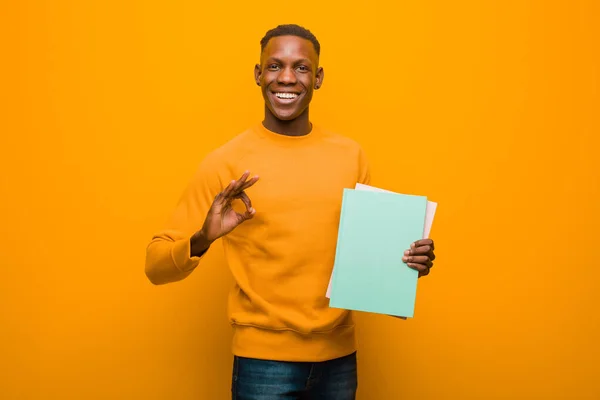 young african american black man against orange wall with a book