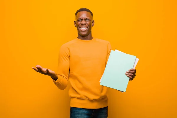 young african american black man against orange wall with a book