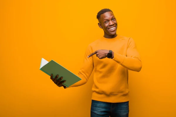young african american black man against orange wall with a book